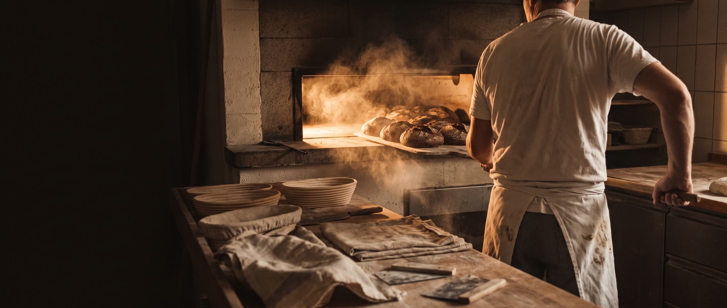 Bäcker schiebt Roggenbrote mit einem Holzschieber in den Steinbackofen